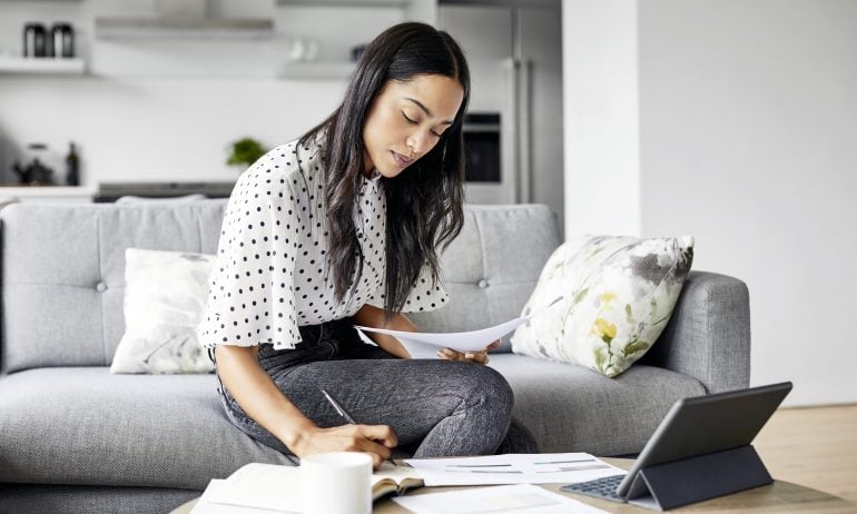 A woman sitting in a living room with papers and a tablet — an image of what learning how to invest money can look like.