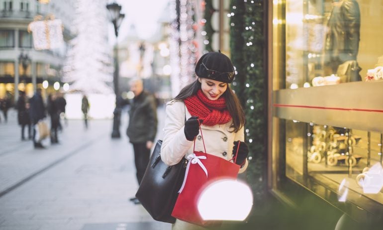 Young woman wearing a red scarf holds a red gift bag in front of a store window