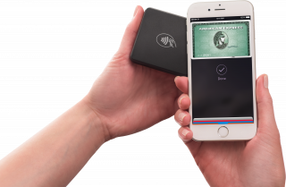 One hand on the right holds up a smartphone to the Payanywhere 3-in-1 reader on the left