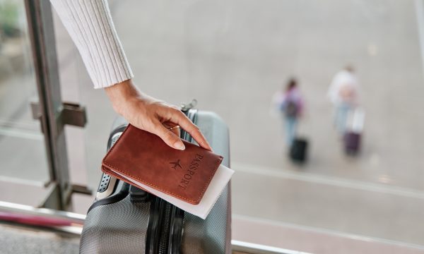 Woman hand with suitcase and passport waiting at airport terminal.