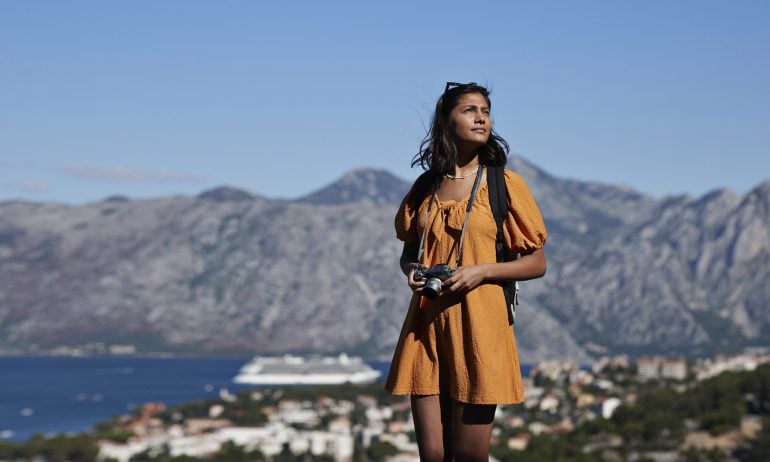 Contemplative young female tourist with camera standing against mountain range on sunny day