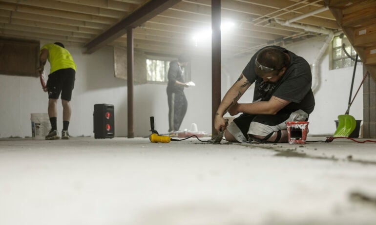 People repairing a basement floor.