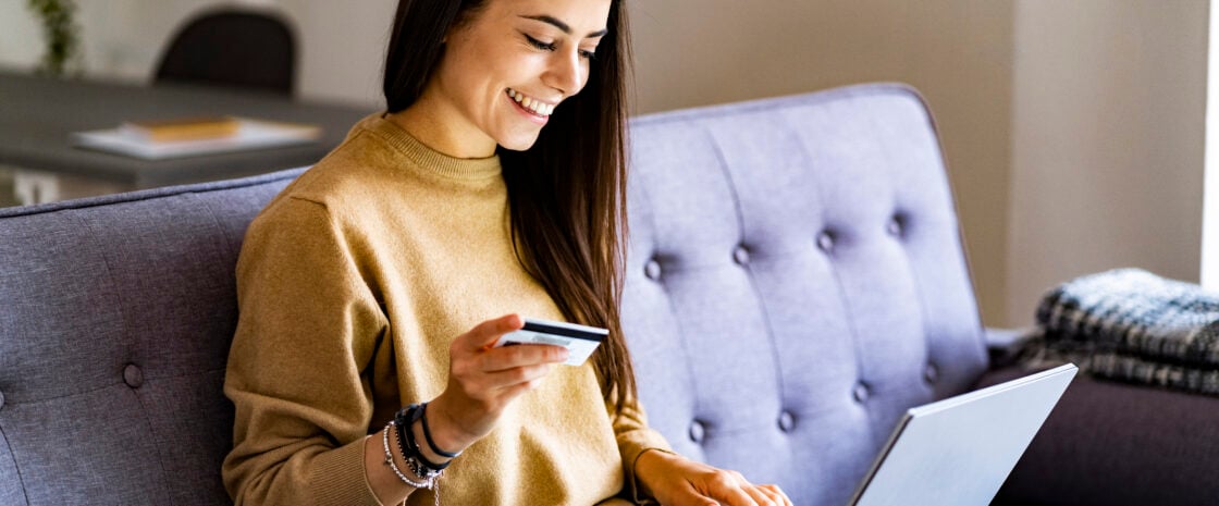 Woman sitting on sofa with her laptop and a credit card.