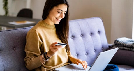 Woman sitting on sofa with her laptop and a credit card.