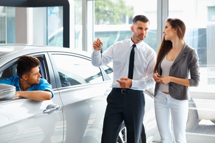 Car Salesman Giving a Key From the New Car to the Young Owners