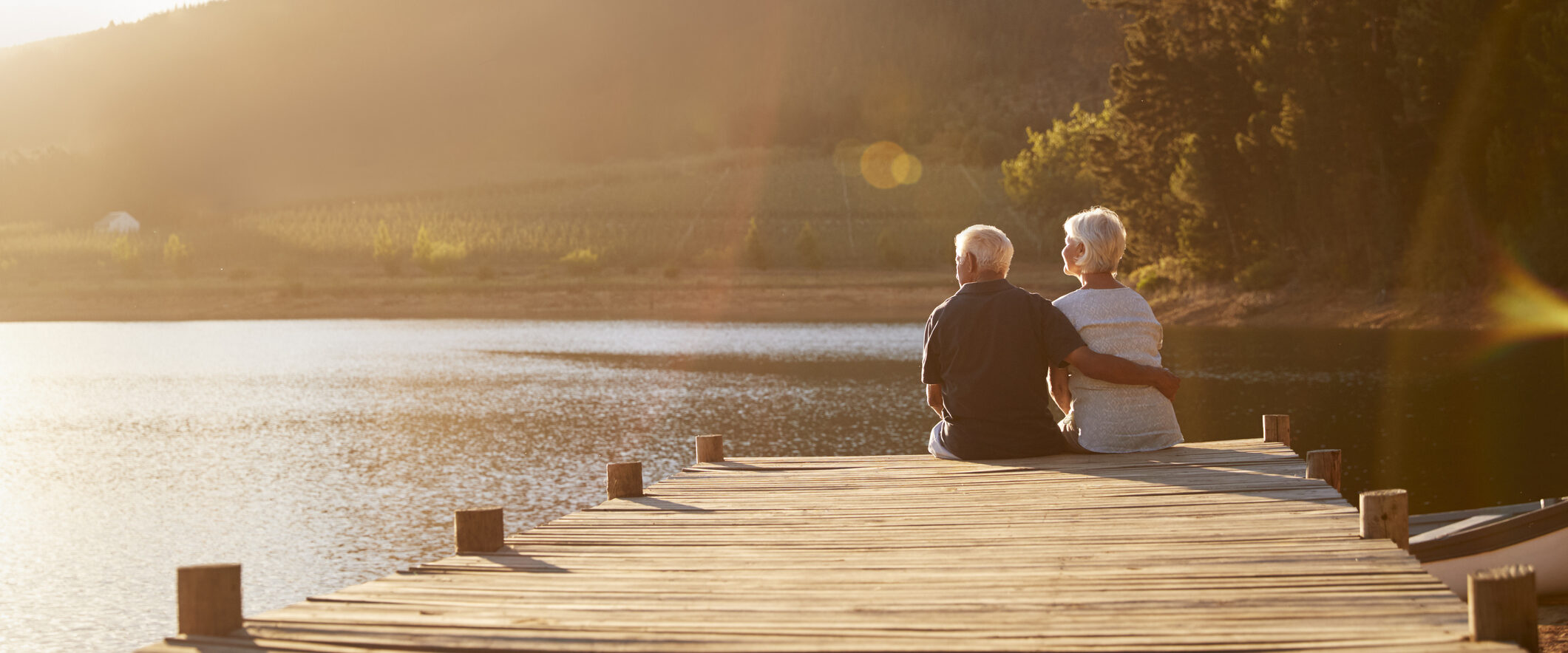 Senior couple sits by lake, enjoying their retirement.