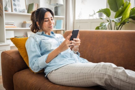 Smiling woman using her bank's mobile app to complete a banking transaction while sitting on her sofa.