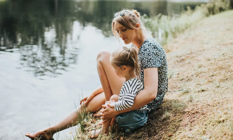 A woman and child sitting on the bank of a river — an abstract representation of basic education, such as investments for beginners.