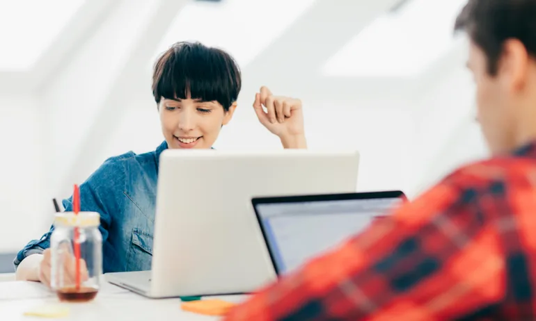 A woman takes notes next to her laptop — a representation of someone learning how to open their Roth IRA.