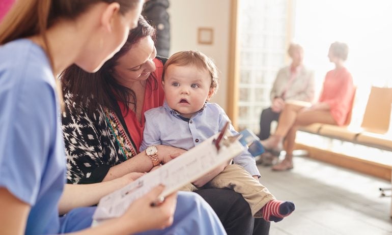 Mom holds a baby boy as they talk with a nurse at a doctor's office