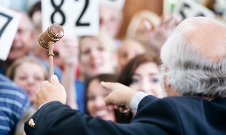 An auctioneer with a gavel points to bidders