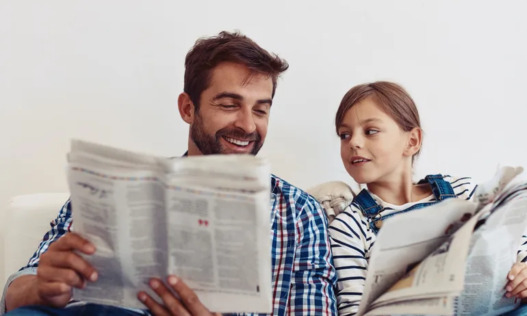 A father and child looking at a newspaper together — an abstract representation of financial education, such as learning how to invest in the S&P 500.