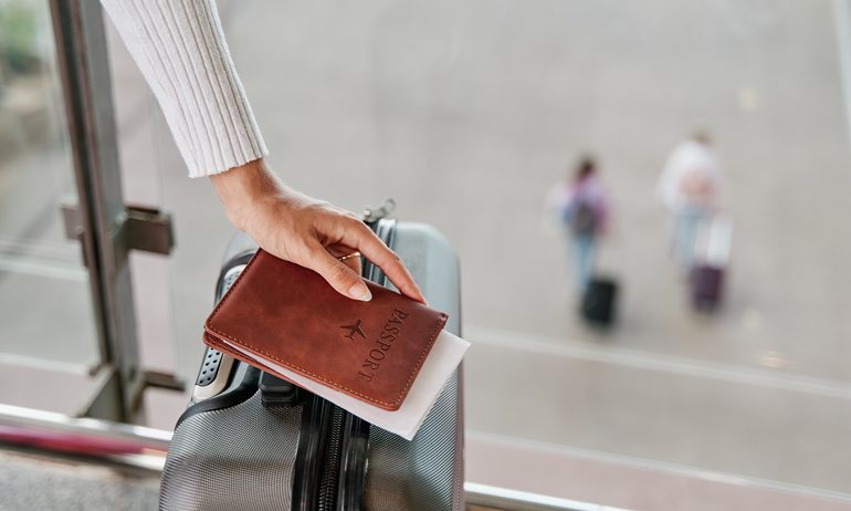 Woman hand with suitcase and passport waiting at airport terminal.