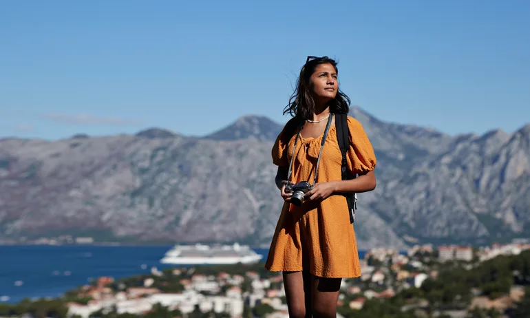 Contemplative young female tourist with camera standing against mountain range on sunny day