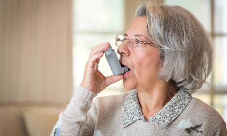 Close up of older Hispanic woman using asthma inhaler