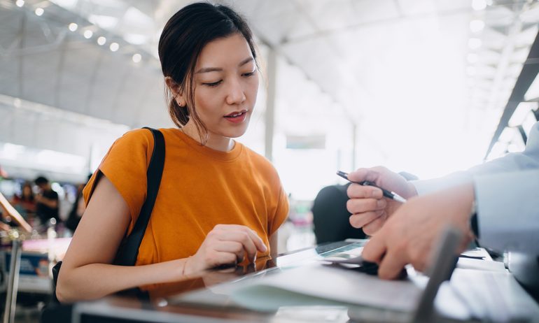 Young Asian woman travelling by airplane and doing check-in at airline check-in counter at airport terminal. Business travel. Travel and vacation concept