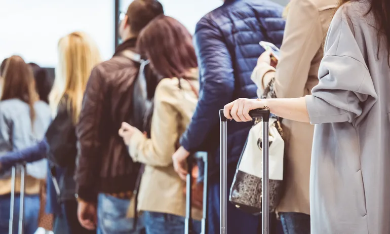 Group of people standing in queue at boarding gate. Focus on female hand holding suitcase handle.