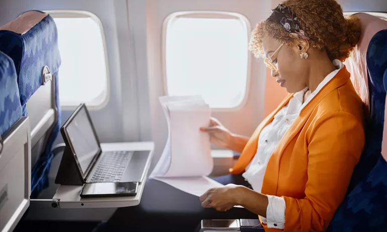 Business travel. Mature businesswoman sitting in an airplane using a laptop.