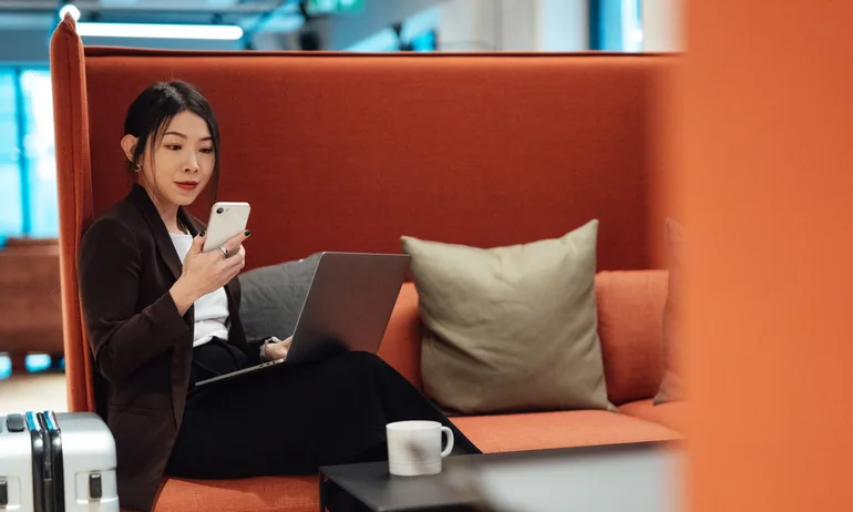 Business woman doing checking emails with smartphone while sitting at airport lounge, getting ready to depart. Young woman on business trip.